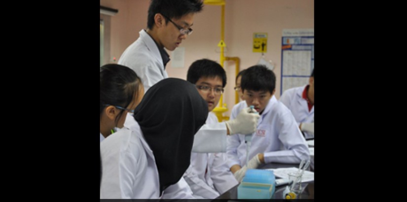 The "FBI Agent" aka BSc Biotech student Felius Yuseli (standing), assisting the student participant group he was assigned to. He is demonstrating how to use a micropipette, an integral equipment of molecular biotechnology.